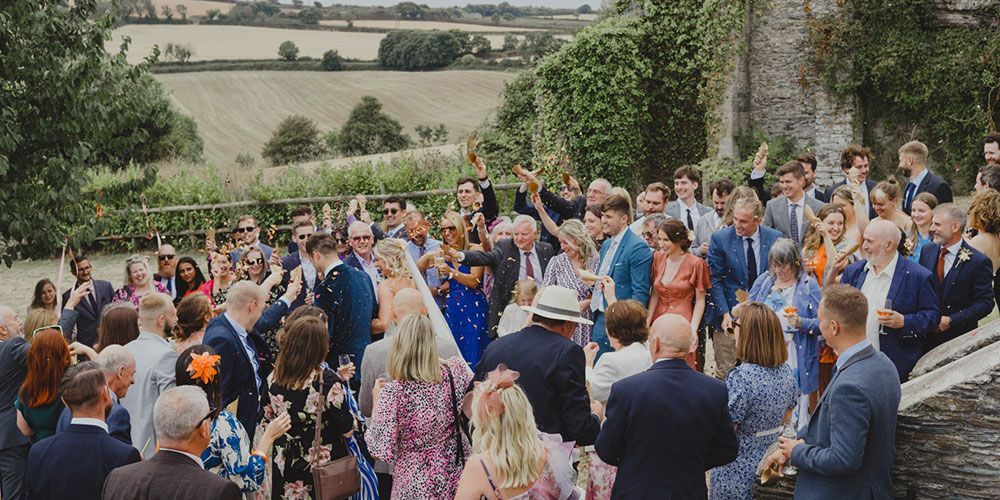 Wedding guests celebrate outdoors, overlooking a field. Bride and groom embraced amid a crowd.