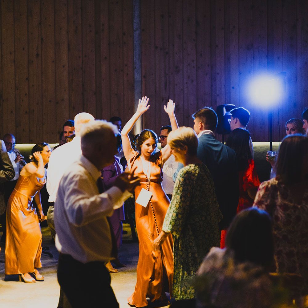People dancing at a party in a wooden-paneled room, woman in orange dress with arms raised.