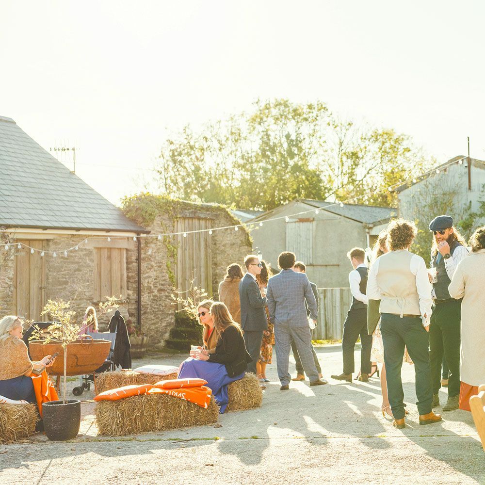 People at an outdoor gathering, sitting on hay bales. Buildings in background, sunny day.