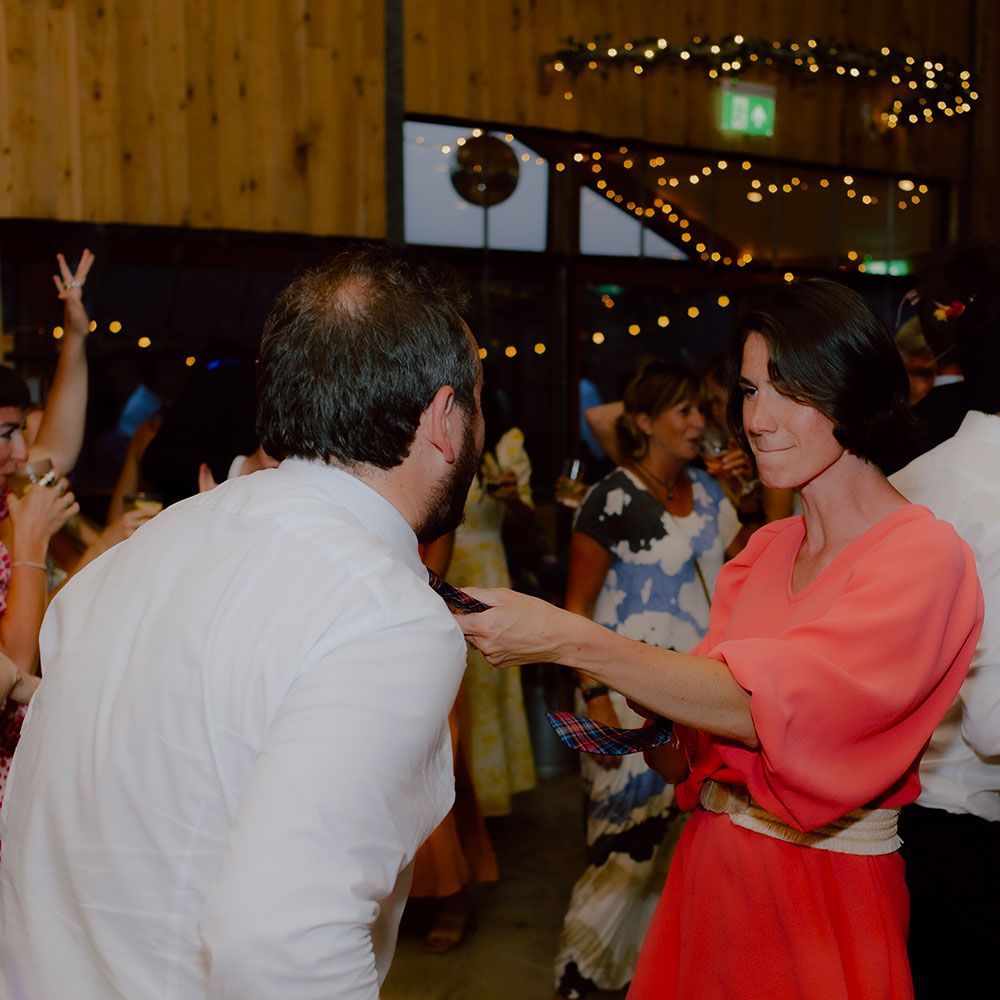 Woman in red dress adjusts man's collar at a party, other people dance in background.