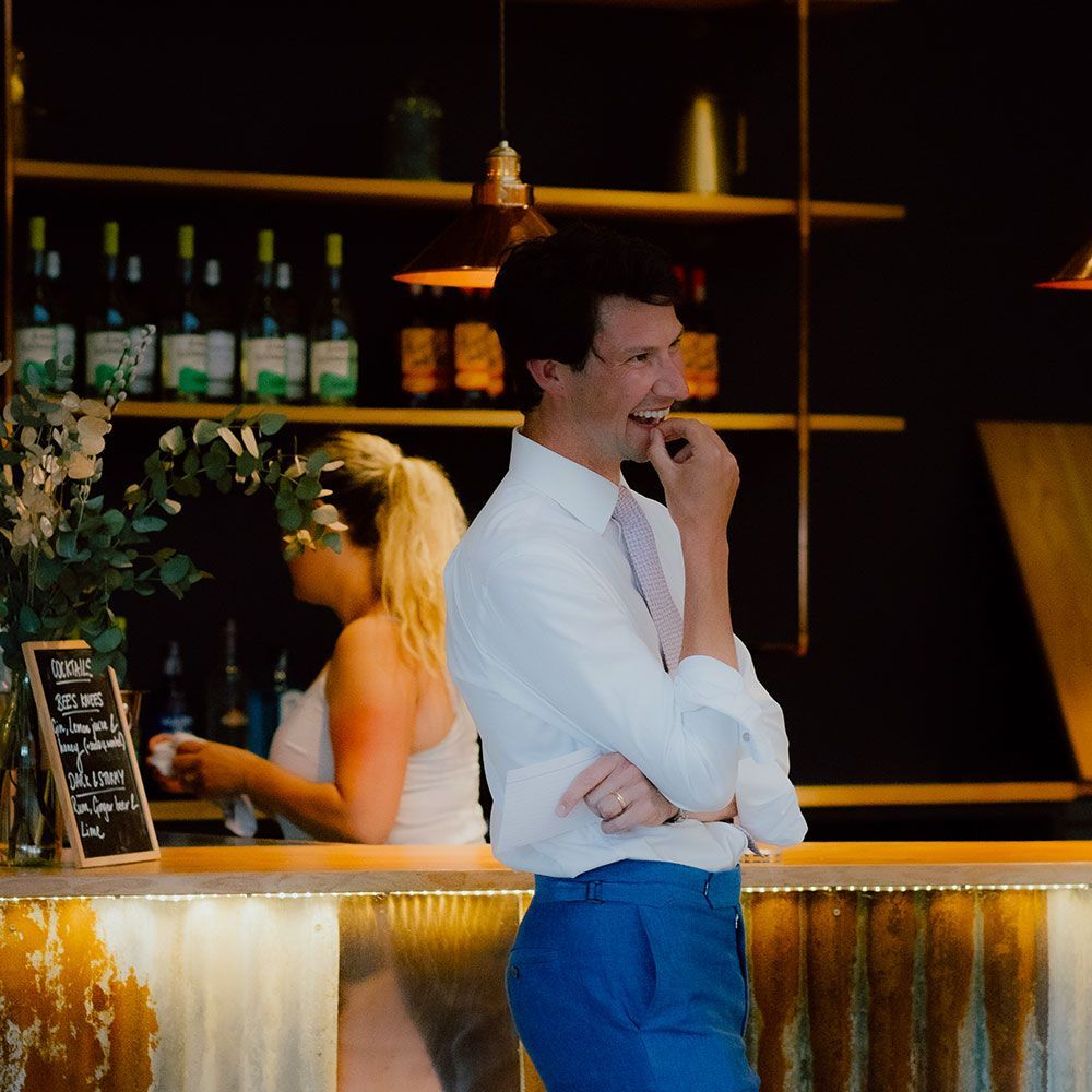 Man in blue pants and white shirt smiles at a bar with a woman behind it.