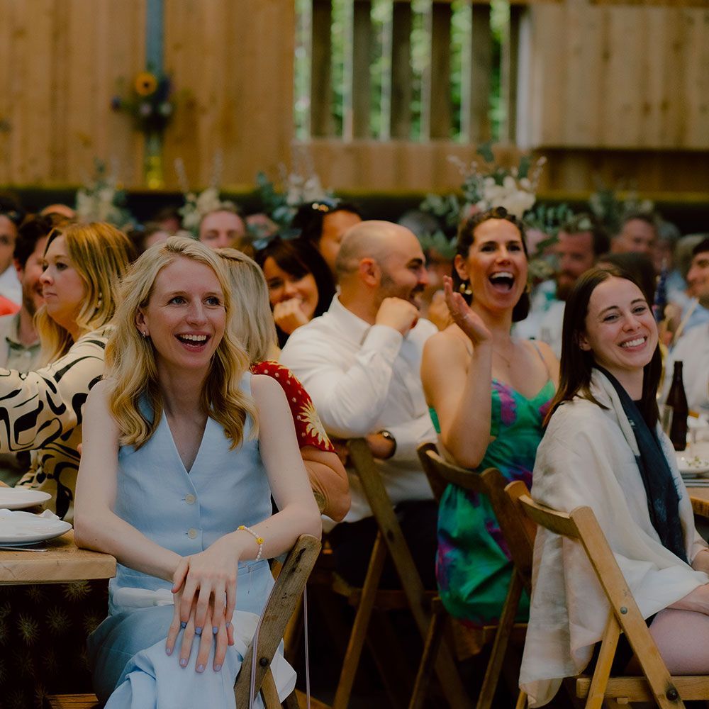 People laughing at a celebration; seated at tables in a rustic, wood-paneled room.