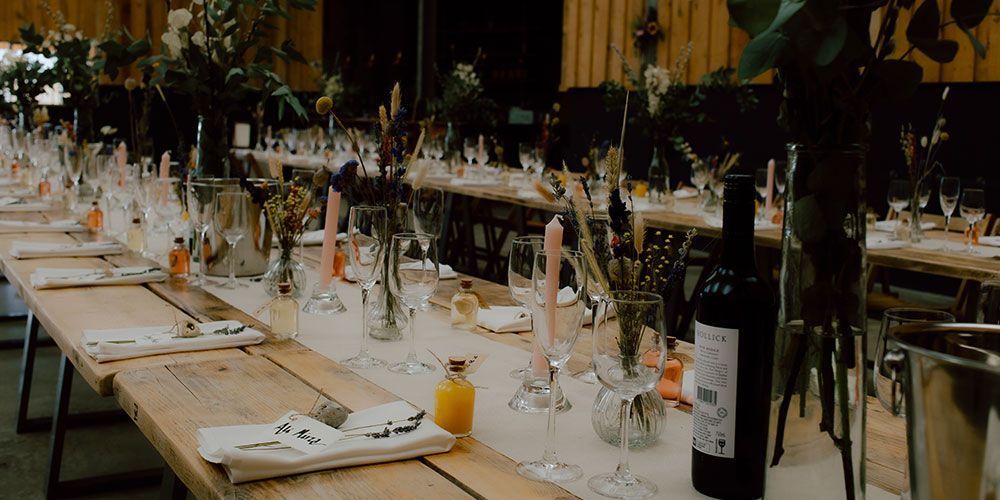Long wooden table set for a wedding reception with floral centerpieces, candles, and wine bottles.