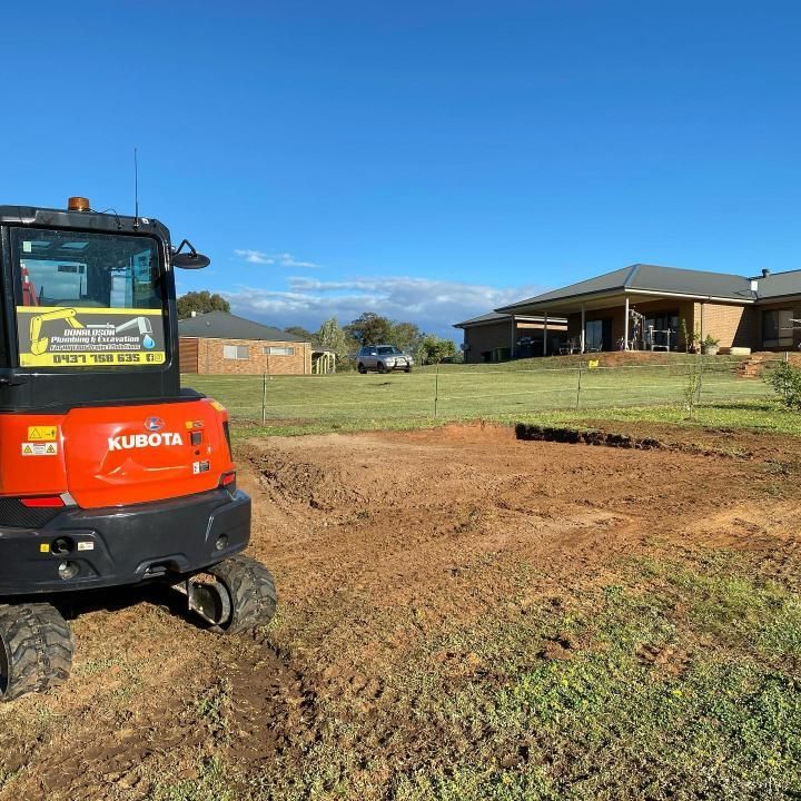 Kubota Excavator is Parked in a Dirt Field in Front of a House — Donaldson Plumbing & Excavations in Albury, NSW