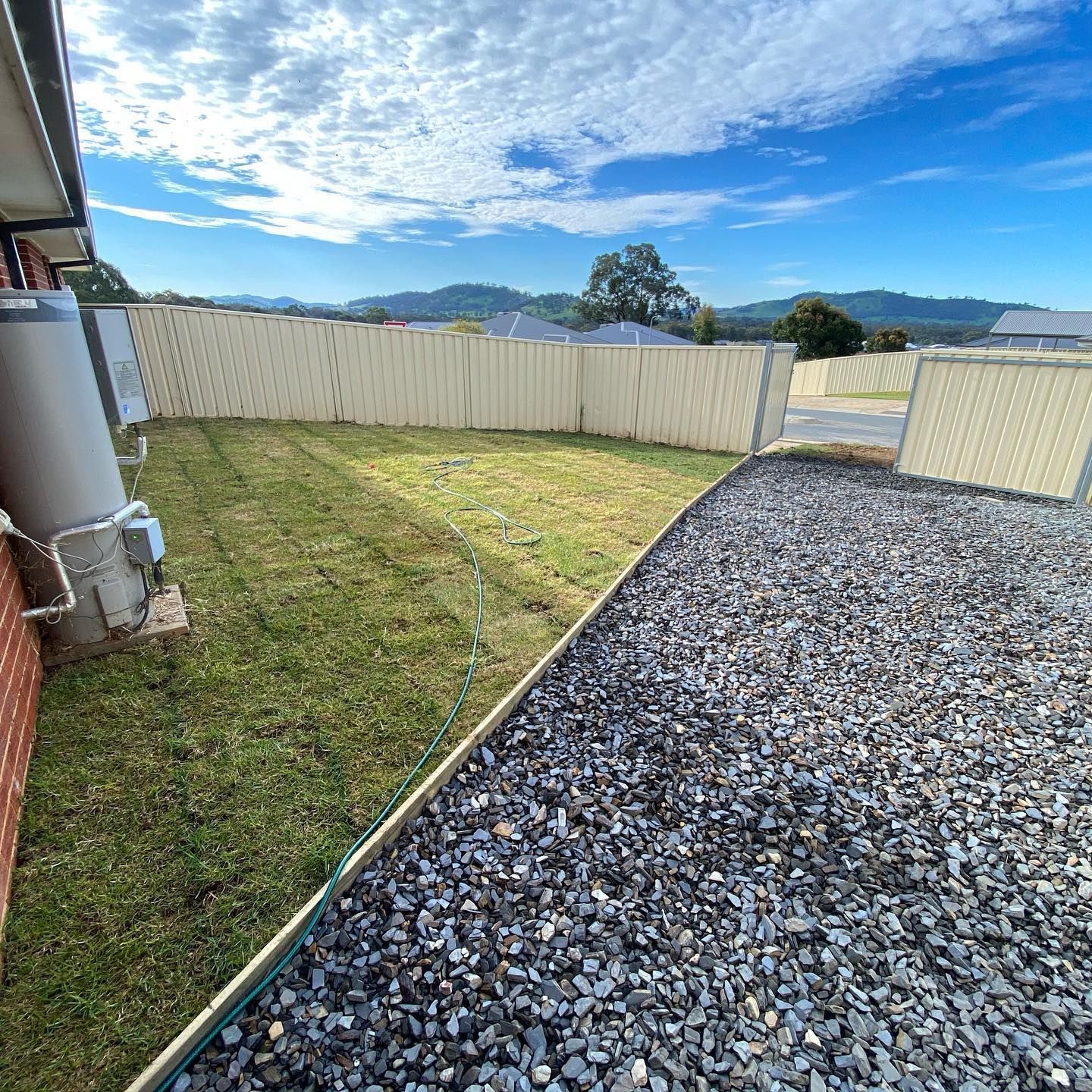 Backyard With a Grassy Lawn, Gravel Driveway, and Beige Fence — Donaldson Plumbing & Excavations in Kiewa, VIC
