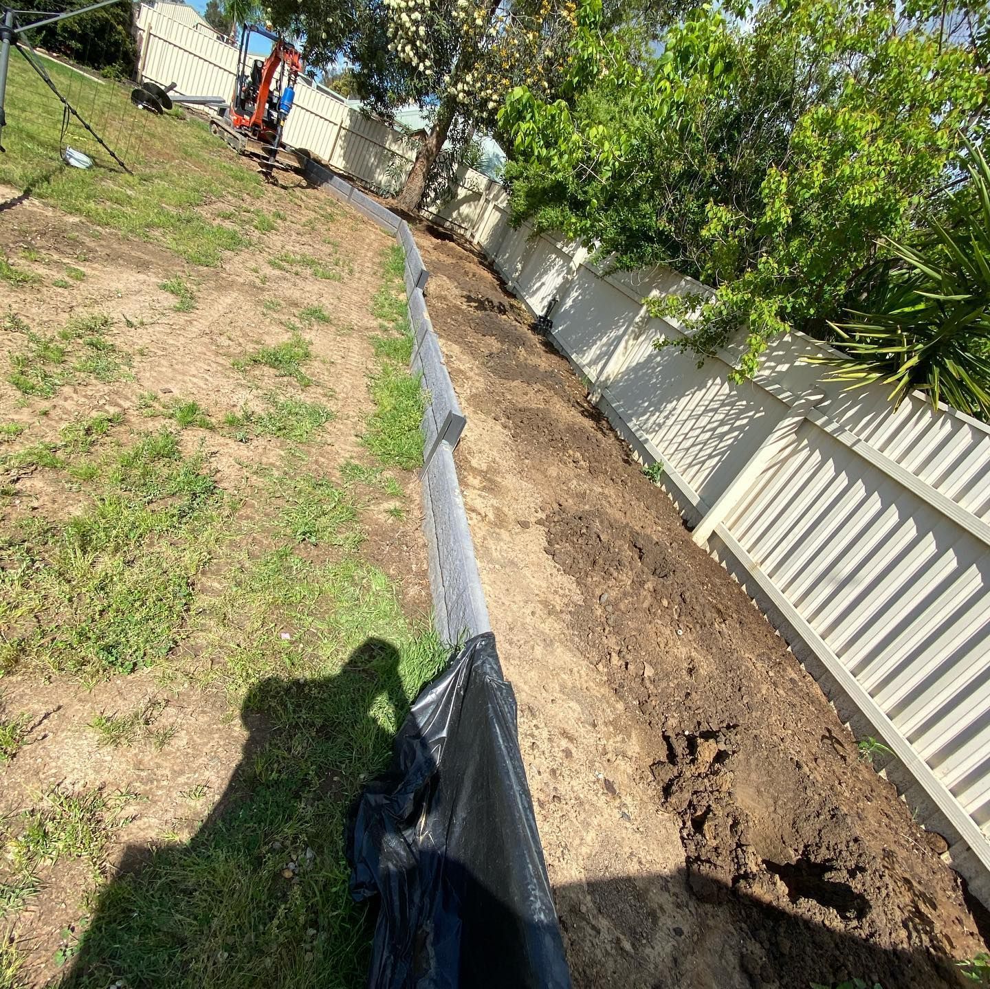 White Fence is Being Built on a Grassy Hillside — Donaldson Plumbing & Excavations in Albury, NSW