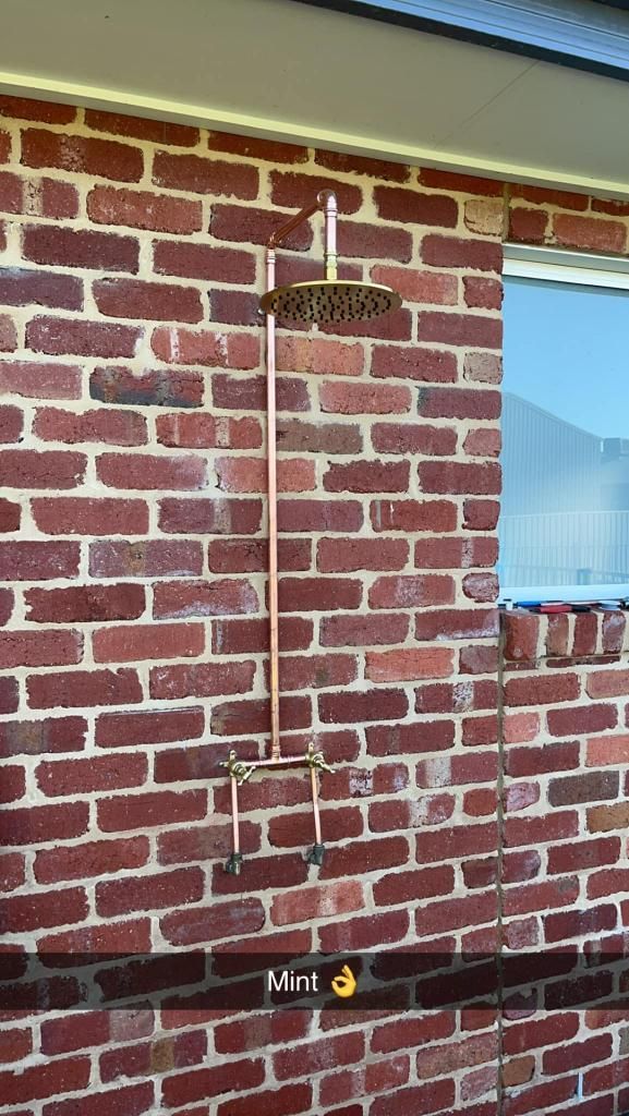 Brick Wall With a Copper Shower Head Attached to It — Donaldson Plumbing & Excavations in Albury, NSW