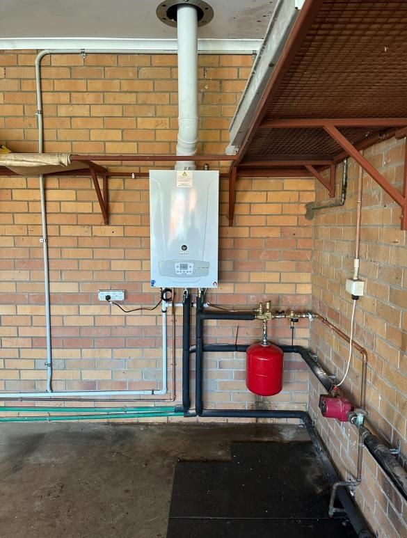 A Gas Boiler With Pipes Against a Brick Wall — Donaldson Plumbing & Excavations in Chiltern, VIC