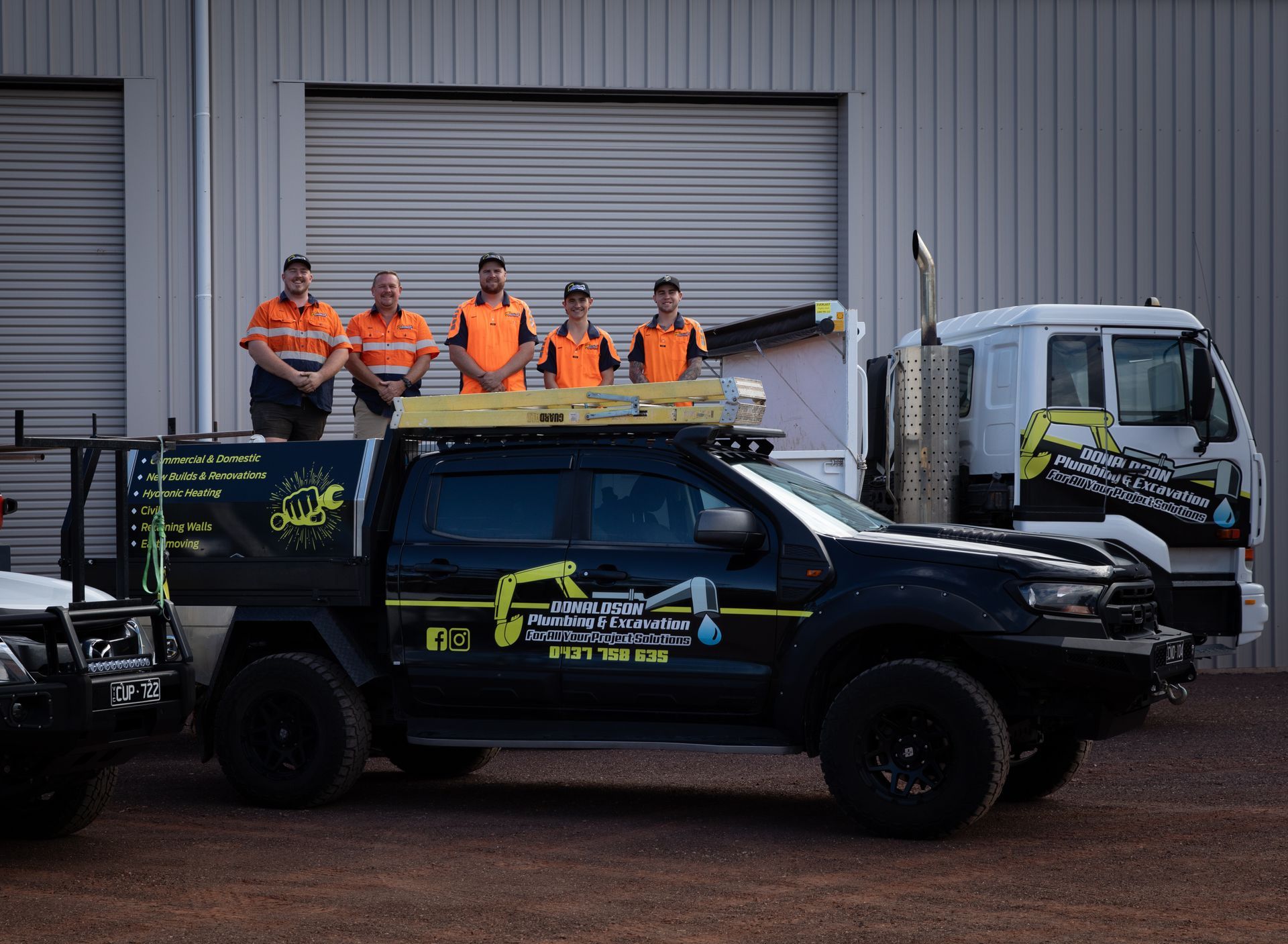 Plumbers Standing With Work Vehicles in Front of a Building — Donaldson Plumbing & Excavations in Baranduda, VIC