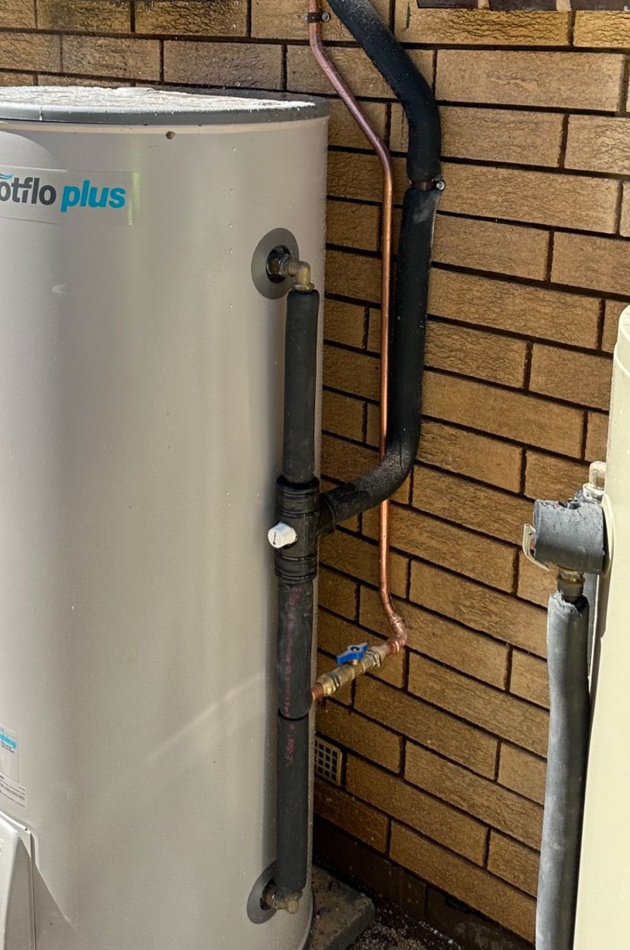 A Hot Water Heater Tank Next to a Brick Wall — Donaldson Plumbing & Excavations in Baranduda, VIC