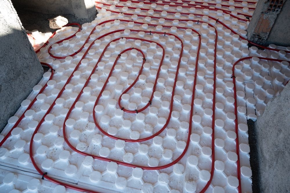 Red tubing laid in a spiral pattern on a white, textured underlayment, likely for radiant floor heating, indoors. — Donaldson Plumbing & Excavations in Wodonga, VIC