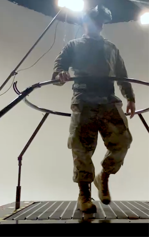 Person in camouflage pants and boots stands on a ship deck under bright overhead lights, holding a rail.