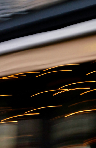 Blurred lights and dark storefronts streak across a moving urban street scene at dusk