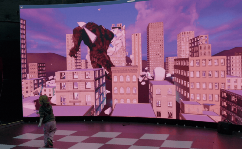Person using a treadmill in a curved indoor VR running setup with a large scenic landscape display.