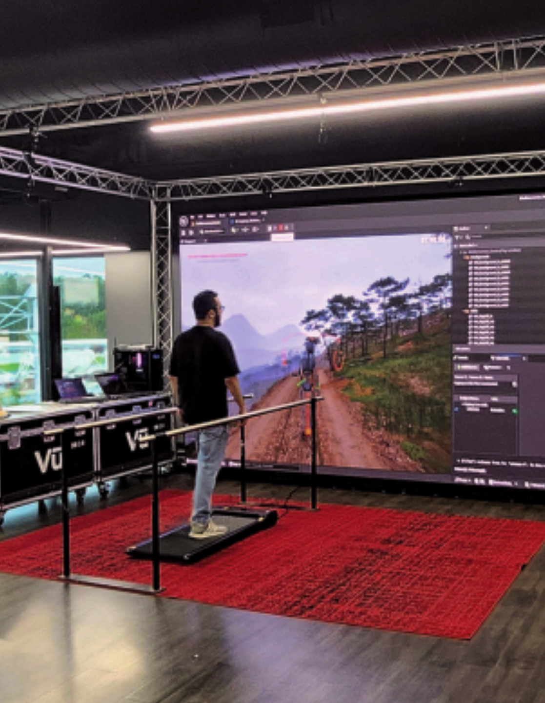 Person viewing a large landscape display in a tech demo booth with red carpet and metal truss lighting