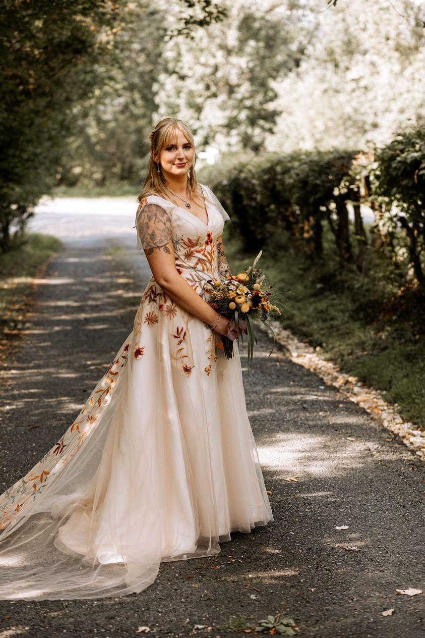 Eine Frau in einem Brautkleid steht mit einem Blumenstrauß in der Hand auf einer Straße.