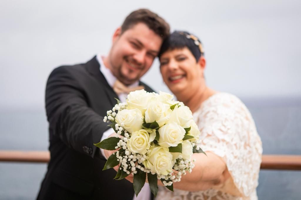 Eine Braut und ein Bräutigam halten einen Strauß weißer Rosen in den Händen.