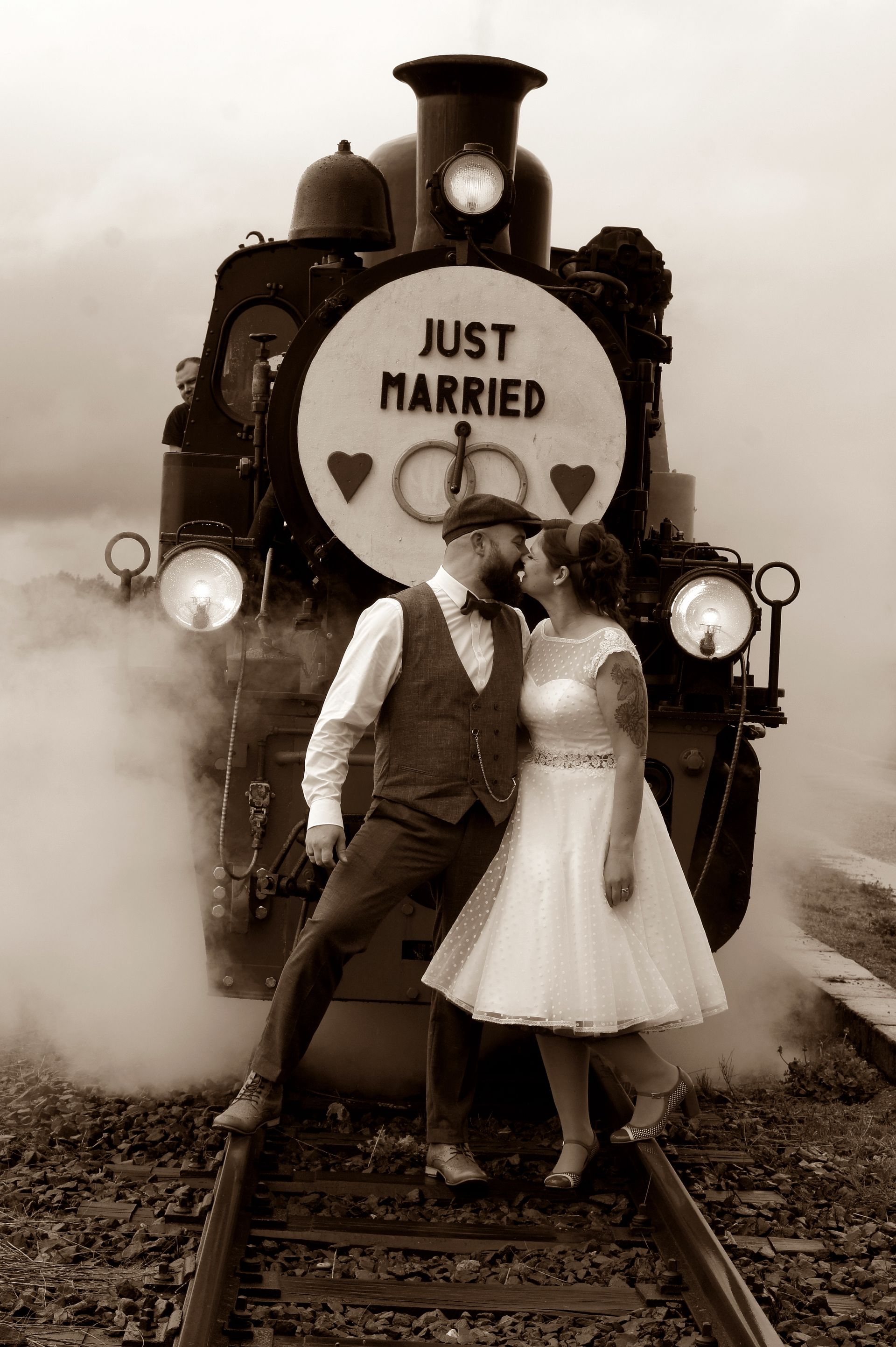 Eine Braut und ein Bräutigam küssen sich vor einem Zug mit der Aufschrift „Just married“.