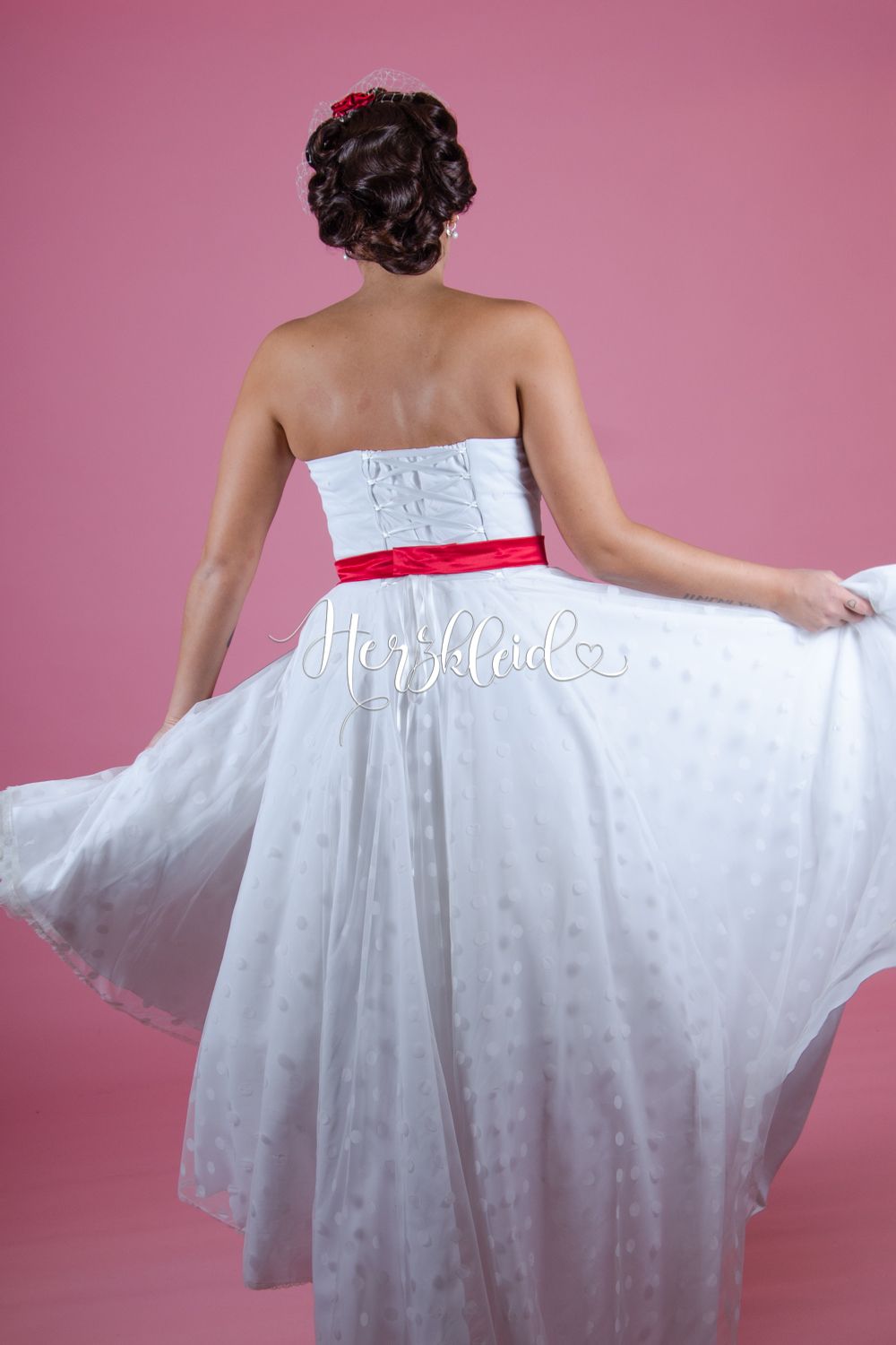 Eine Frau trägt ein weißes Kleid mit einer roten Schleife um die Taille.