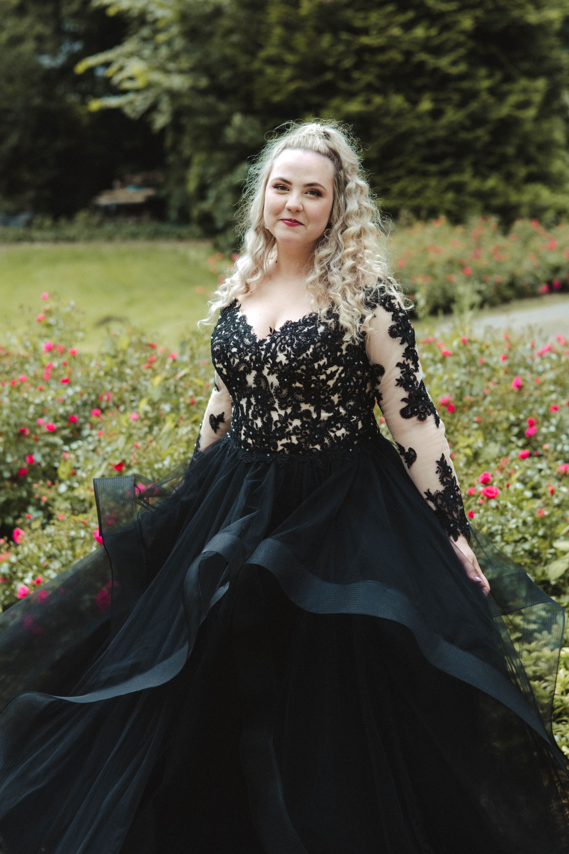 Eine Frau in einem schwarzen Kleid steht in einem Blumenfeld.