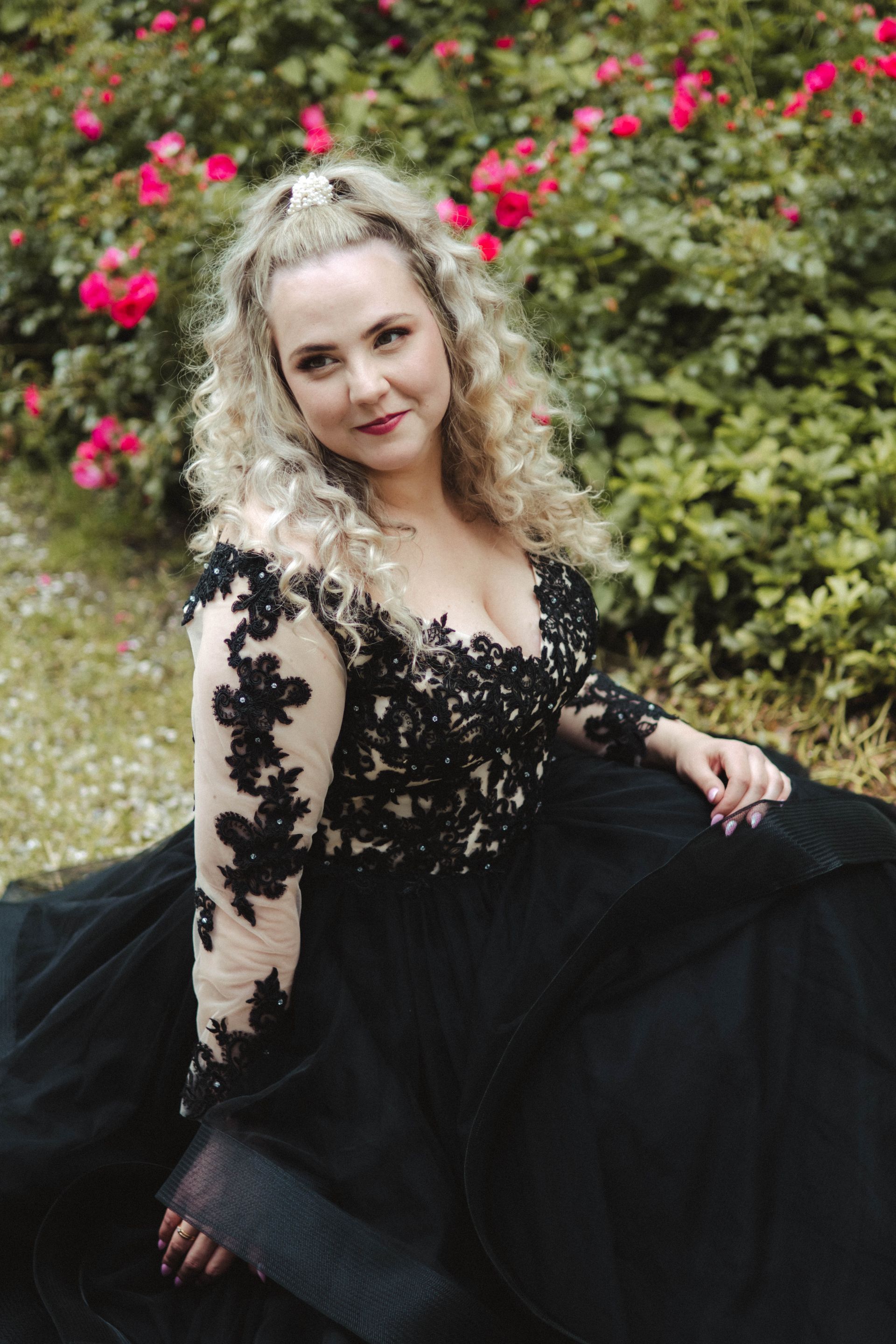 Eine Frau in einem schwarzen Kleid sitzt vor einem Rosenbusch.