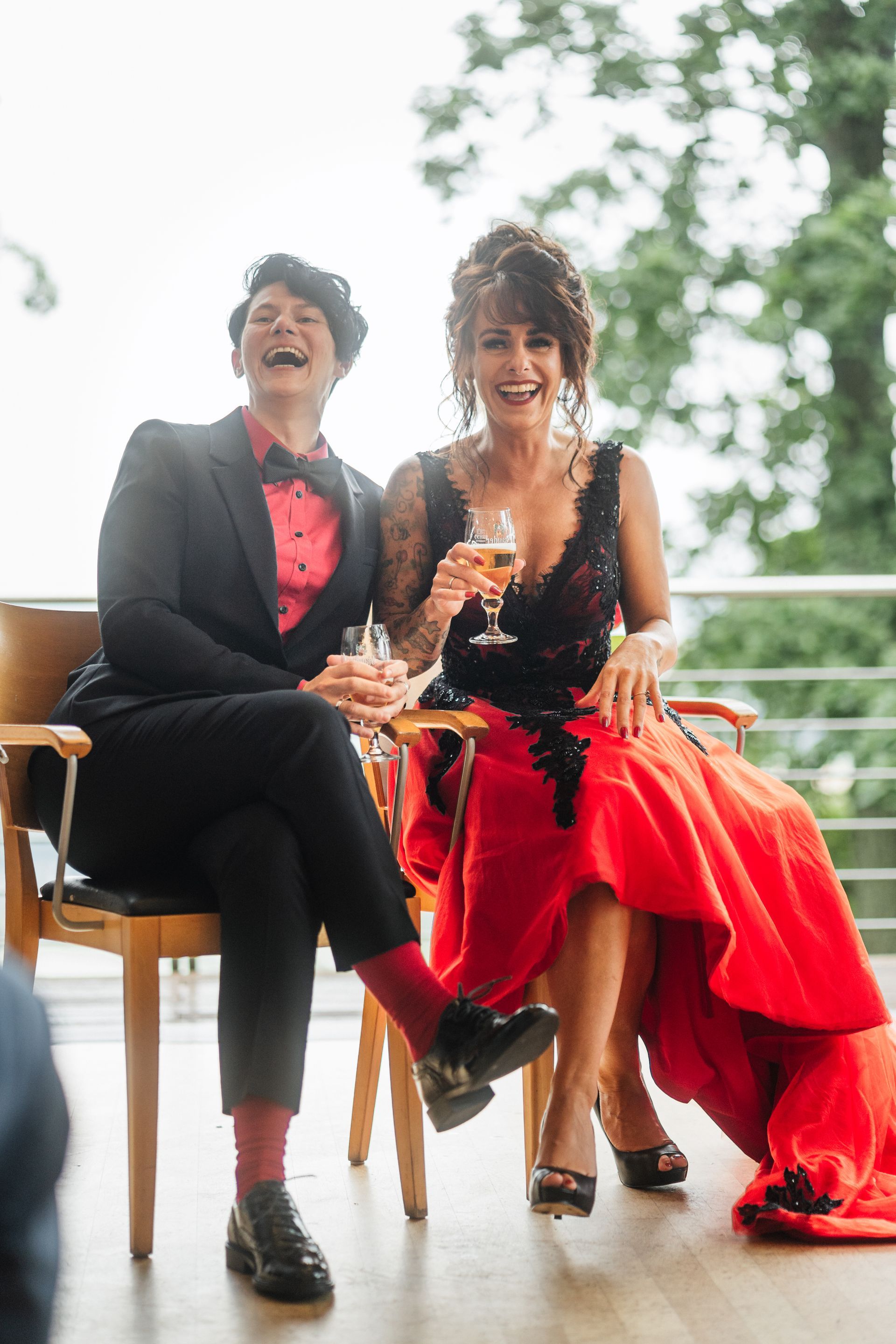 Zwei Frauen sitzen auf Stühlen, halten Champagnergläser und lachen.