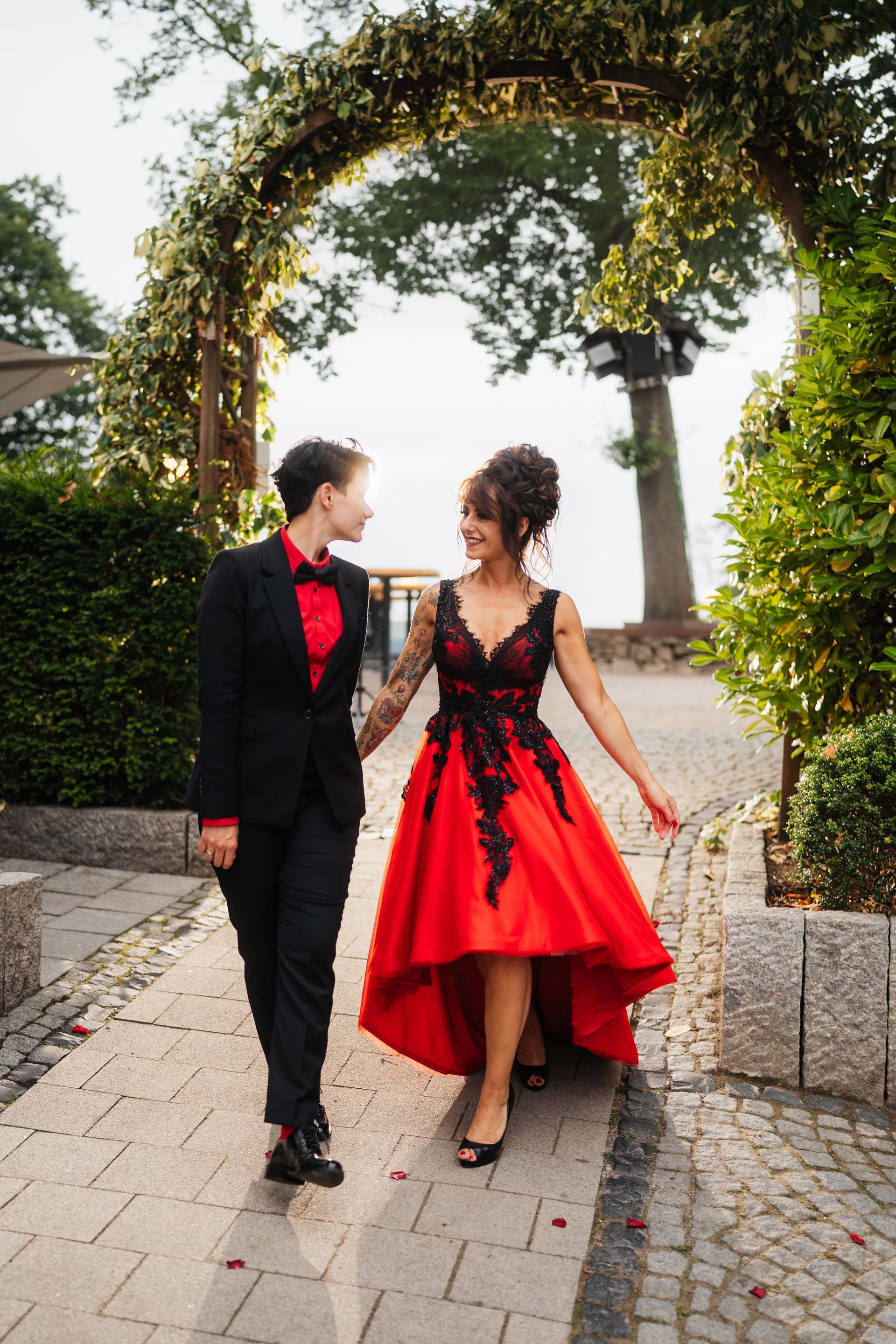 Ein Mann im Smoking und eine Frau in einem roten Kleid gehen einen Bürgersteig entlang.