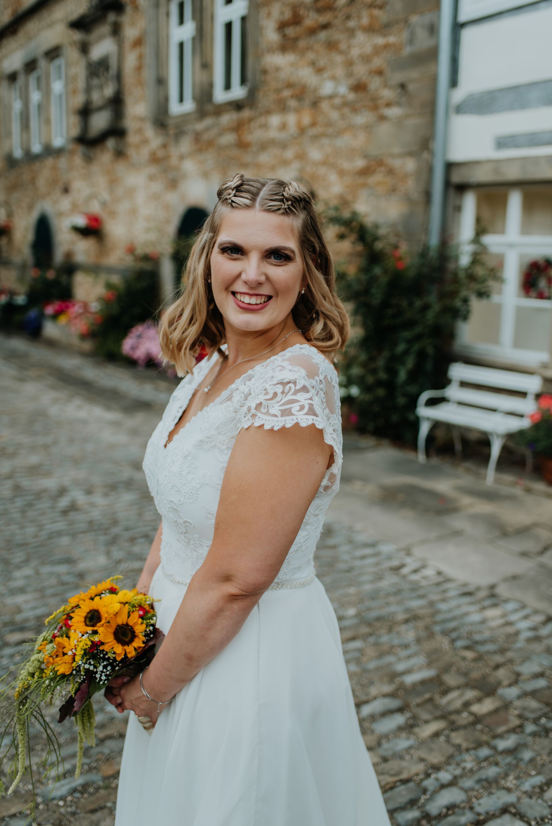 Die Braut trägt ein weißes Kleid und hält einen Strauß Sonnenblumen in der Hand.