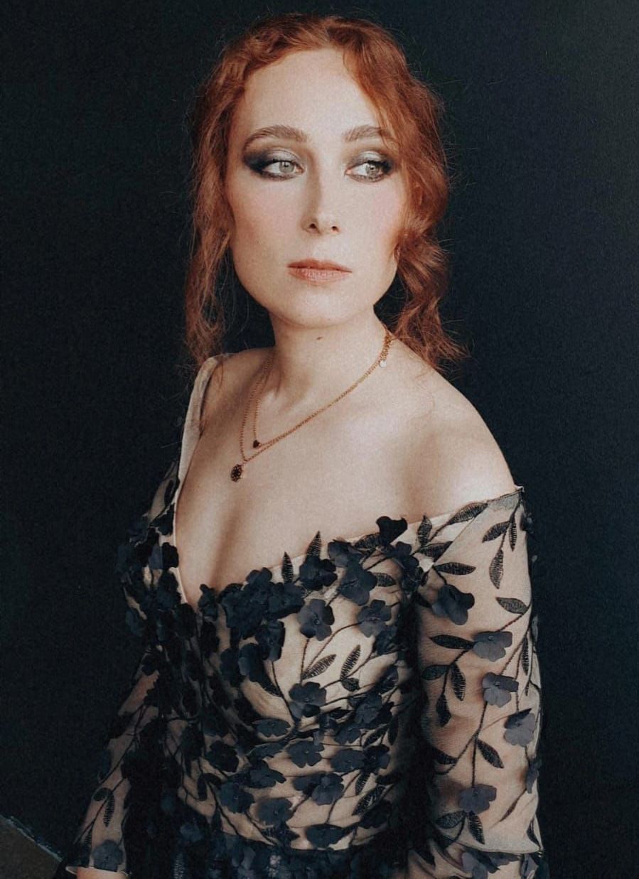 Eine Frau mit roten Haaren trägt ein schwarzes Kleid und eine Halskette.