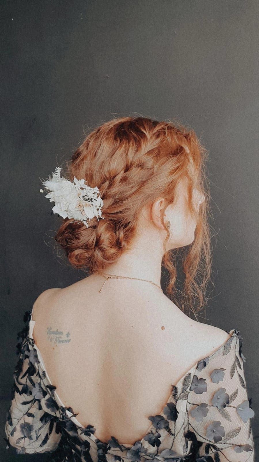 Eine Frau mit roten Haaren trägt einen geflochtenen Dutt mit einer Blume im Haar.