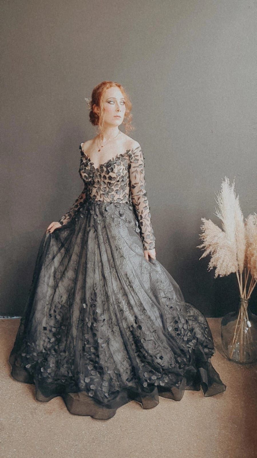 Eine Frau in einem schwarzen Kleid steht neben einer Vase mit Pampasgras.