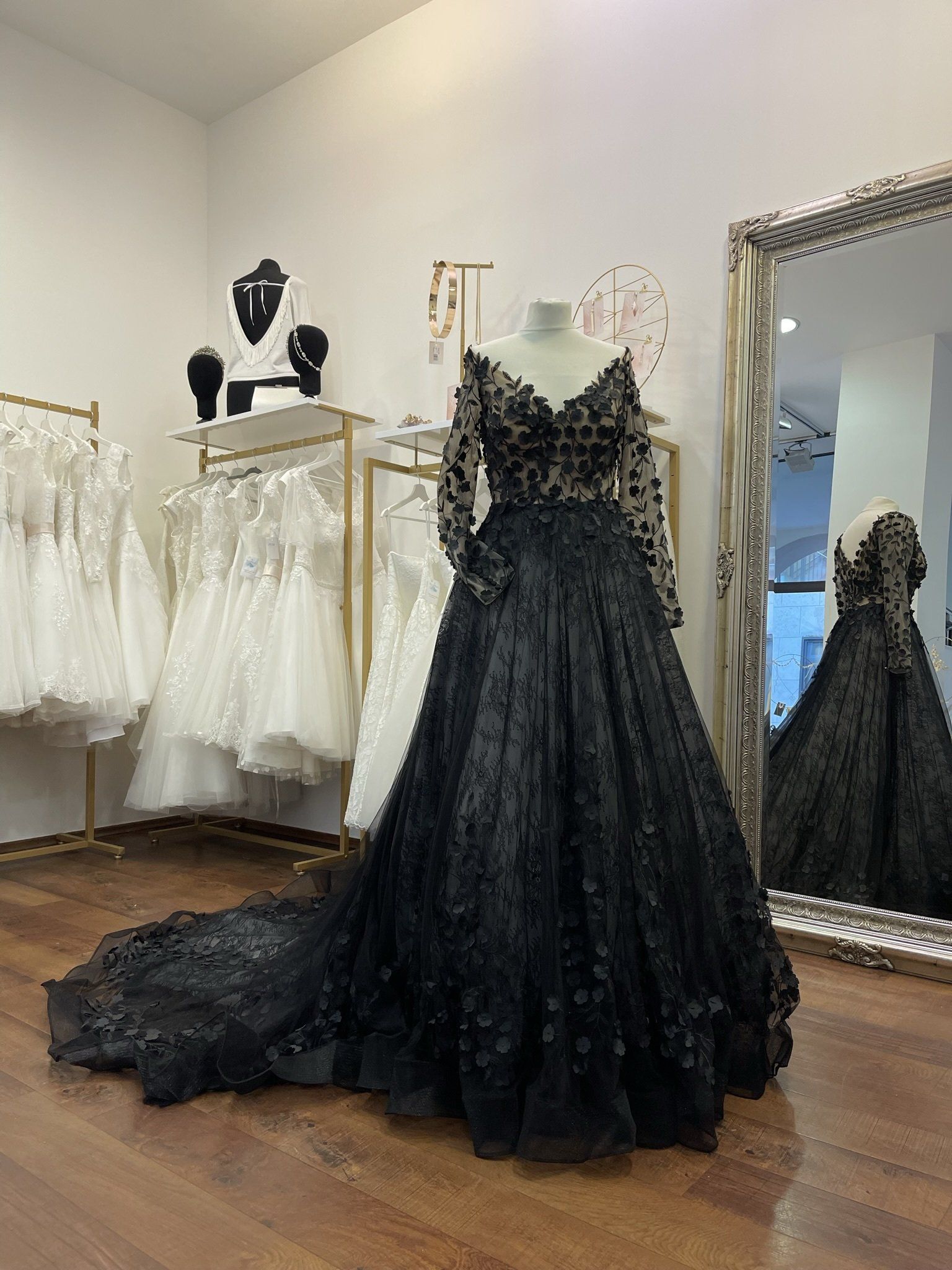 Ein schwarzes Brautkleid hängt auf einer Schaufensterpuppe in einem Raum neben einem Spiegel.