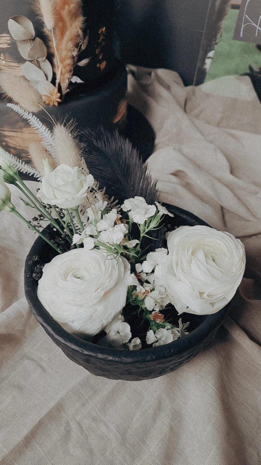 Auf einem Tisch steht eine schwarze Schale mit weißen Blumen.
