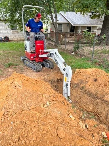 Man operates mini excavator digging trench in yard.