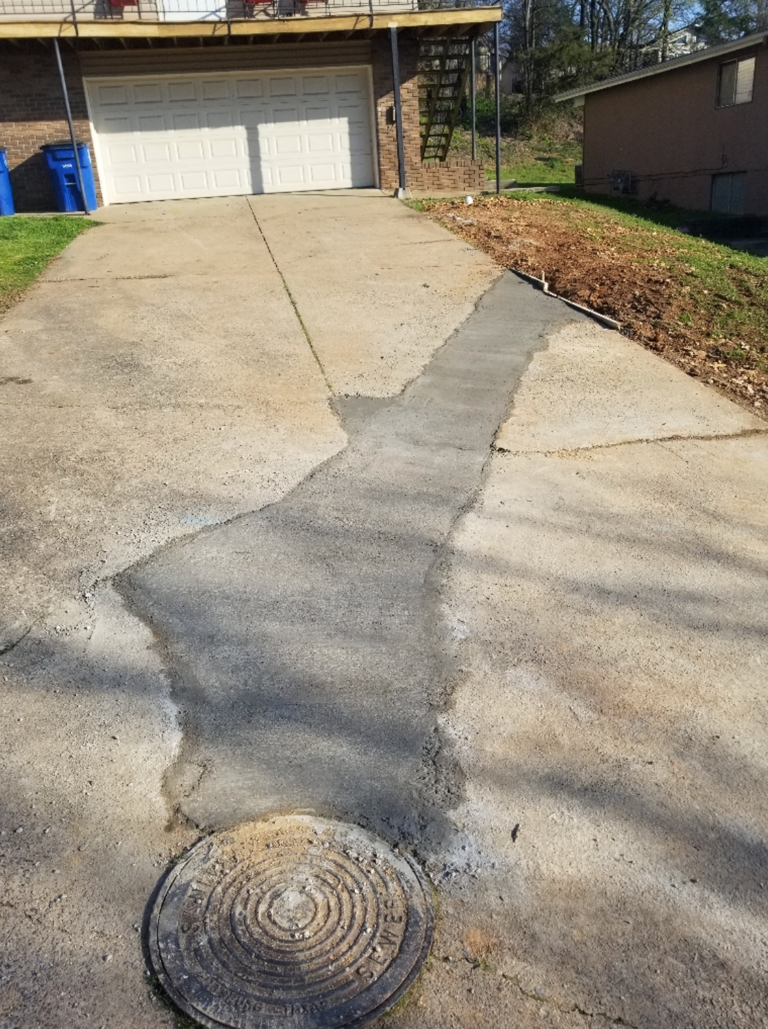 Concrete driveway with a patch, leading to a garage and topped with a metal sewer cover.