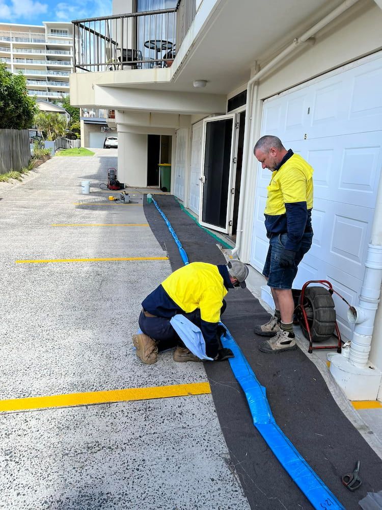 Two Men Are Working on a Blue Pipe in a Parking Lot — FlowWise in Maroochydore, QLD