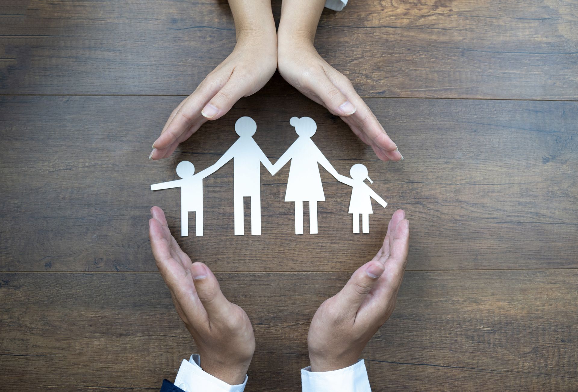 Hands cradling a paper cutout family, symbolizing protection and care.