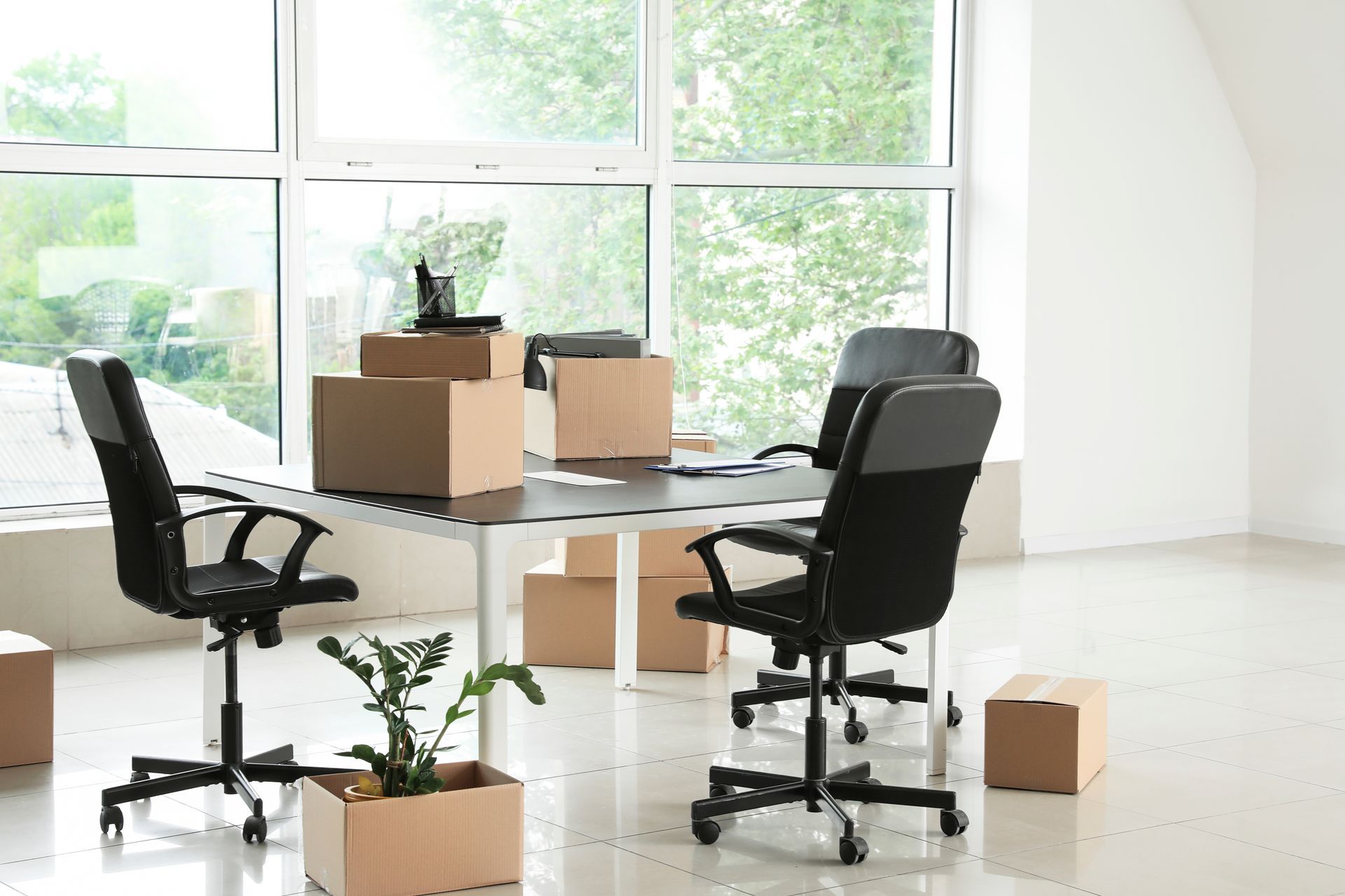 Packed moving boxes and a plant beside an office table and chairs during a commercial relocation