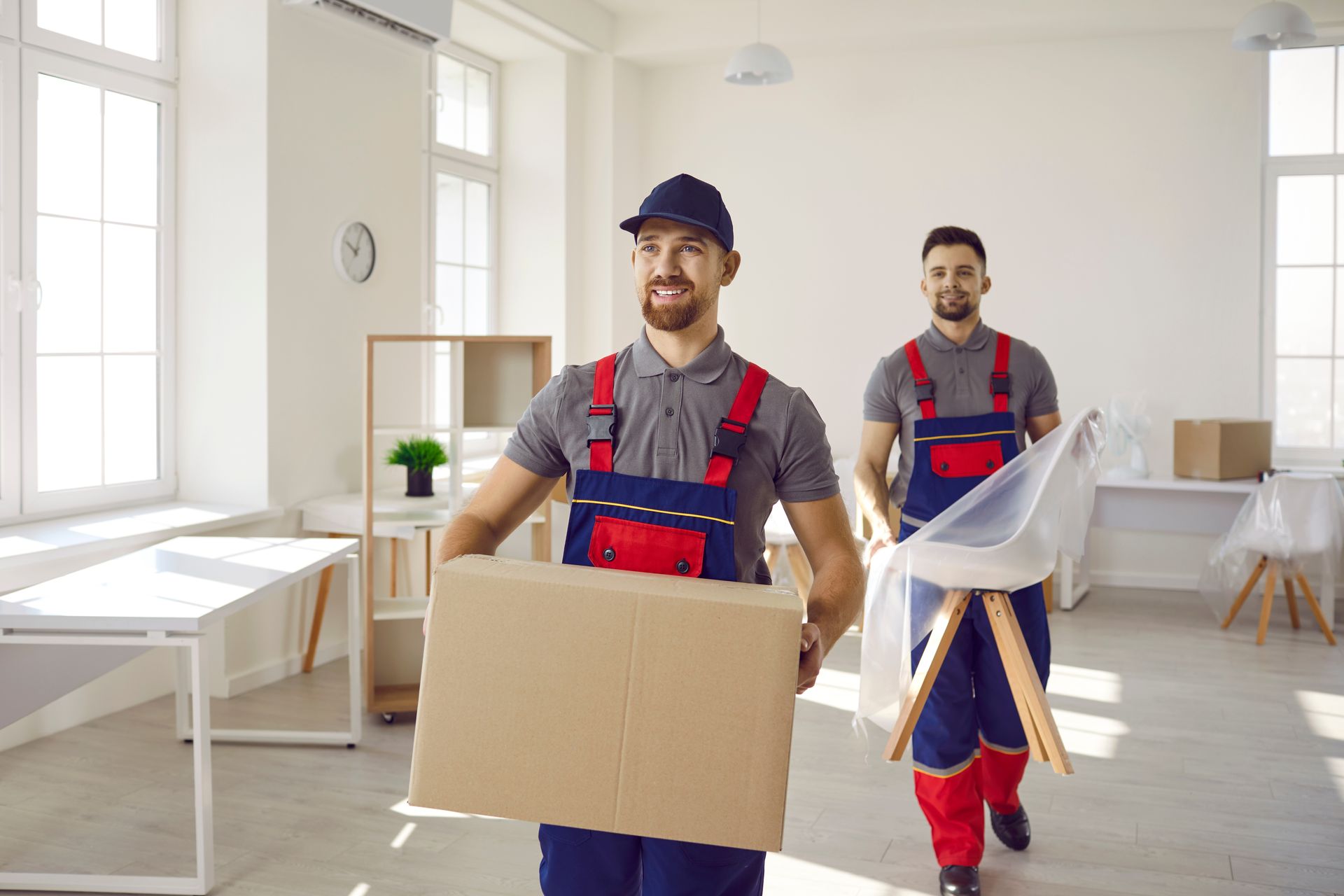 Two movers carrying boxes in a bright, empty room