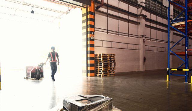 Worker pulling cart from warehouse doorway; light floods in.