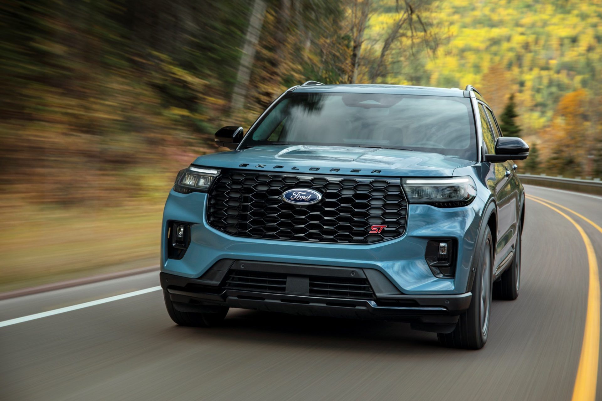 Blue SUV driving on a winding road with autumn trees in the background