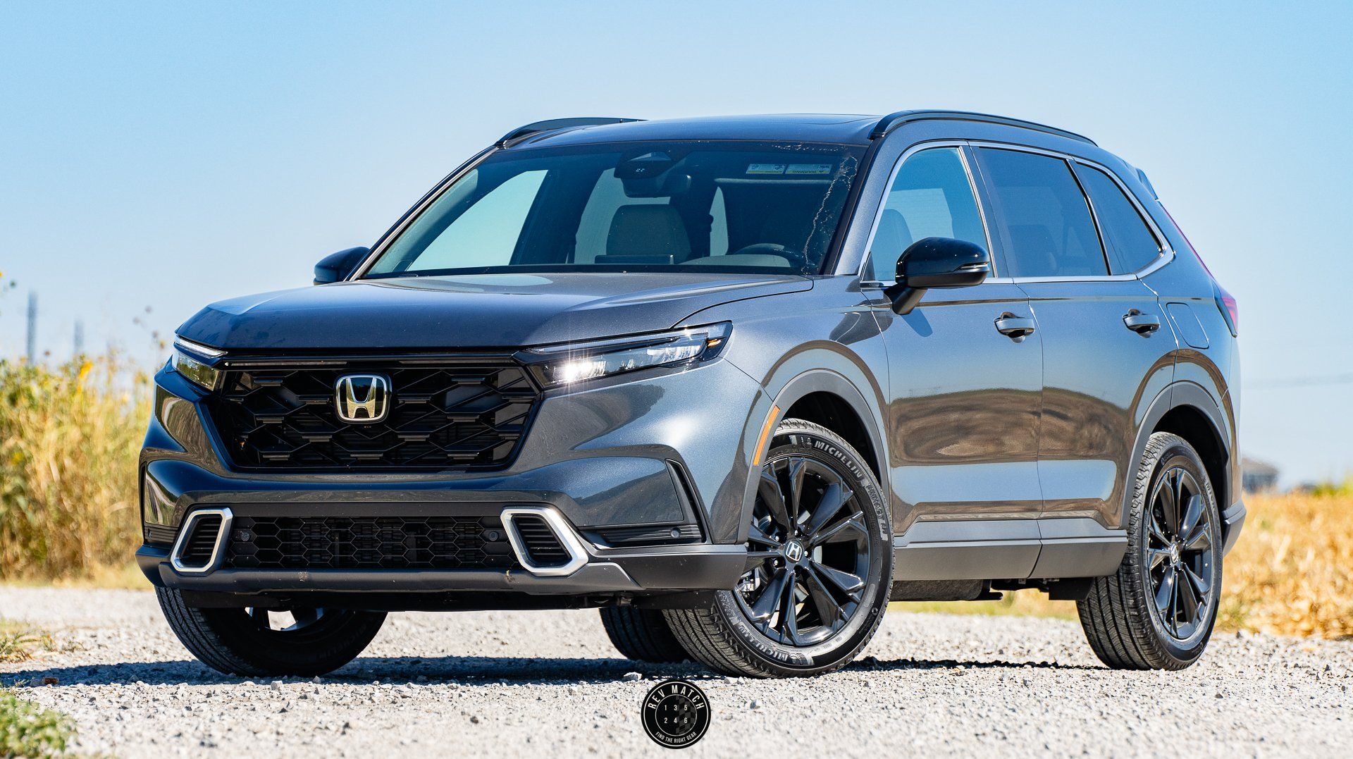 Dark gray Honda SUV parked on a gravel road under a clear blue sky