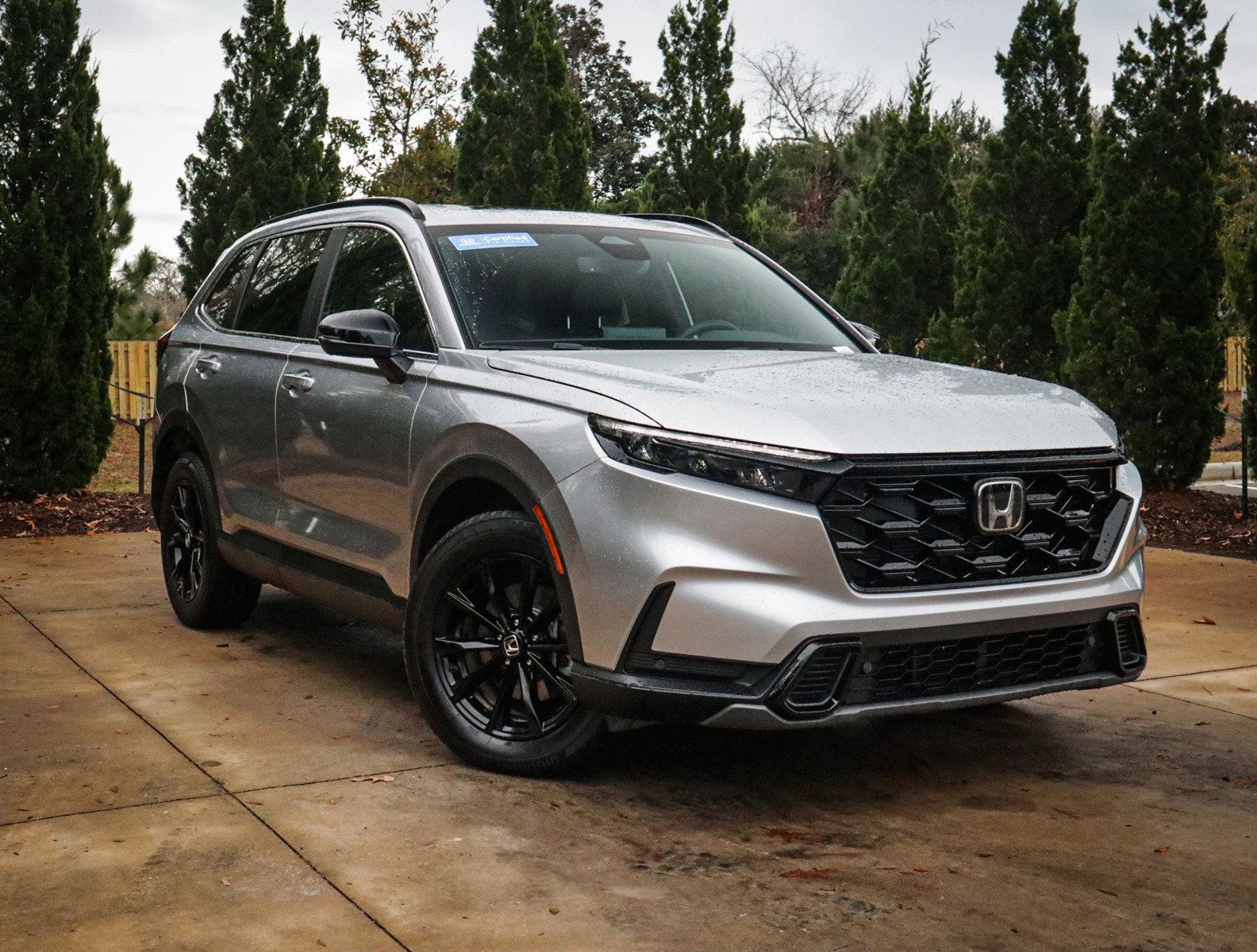 Silver Honda SUV parked on a wet driveway with trees in the background