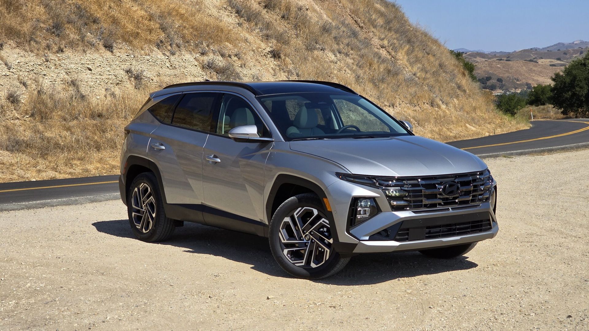Silver SUV on a winding road beside dry hills under clear sky