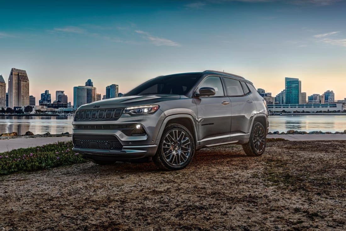 Gray SUV parked by a waterfront with a city skyline at sunset