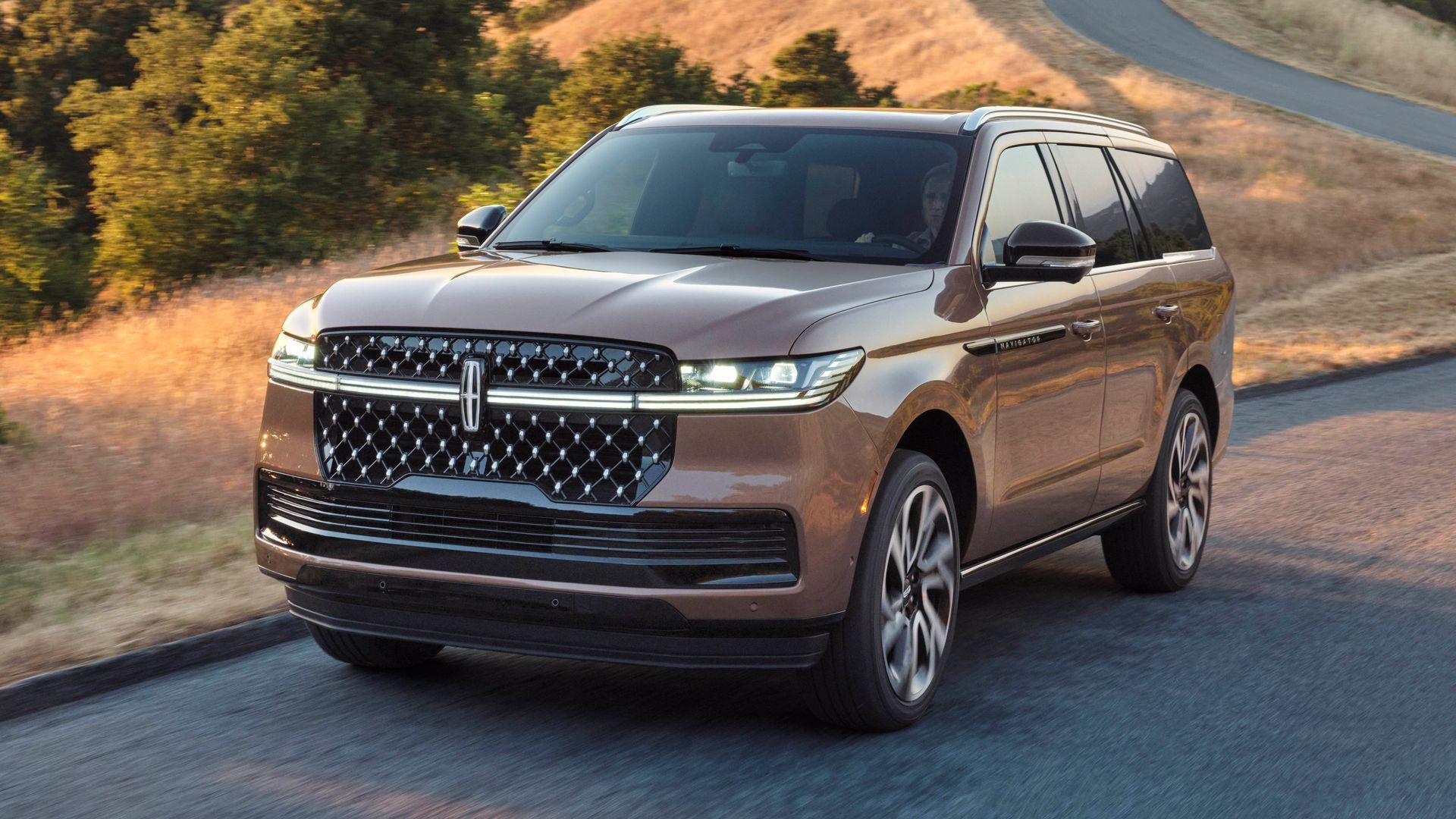 Brown SUV driving on a winding road through a wooded landscape