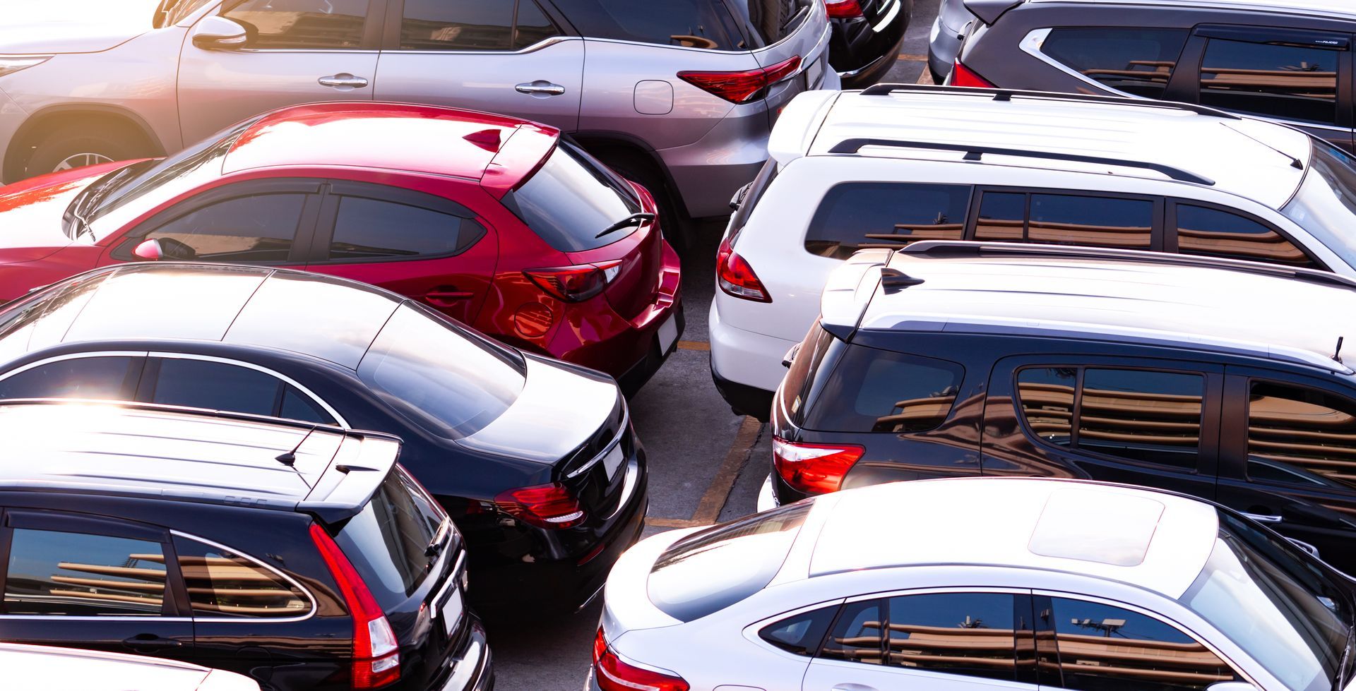 Overhead view of several parked cars in white, black, and red, tightly packed in a lot