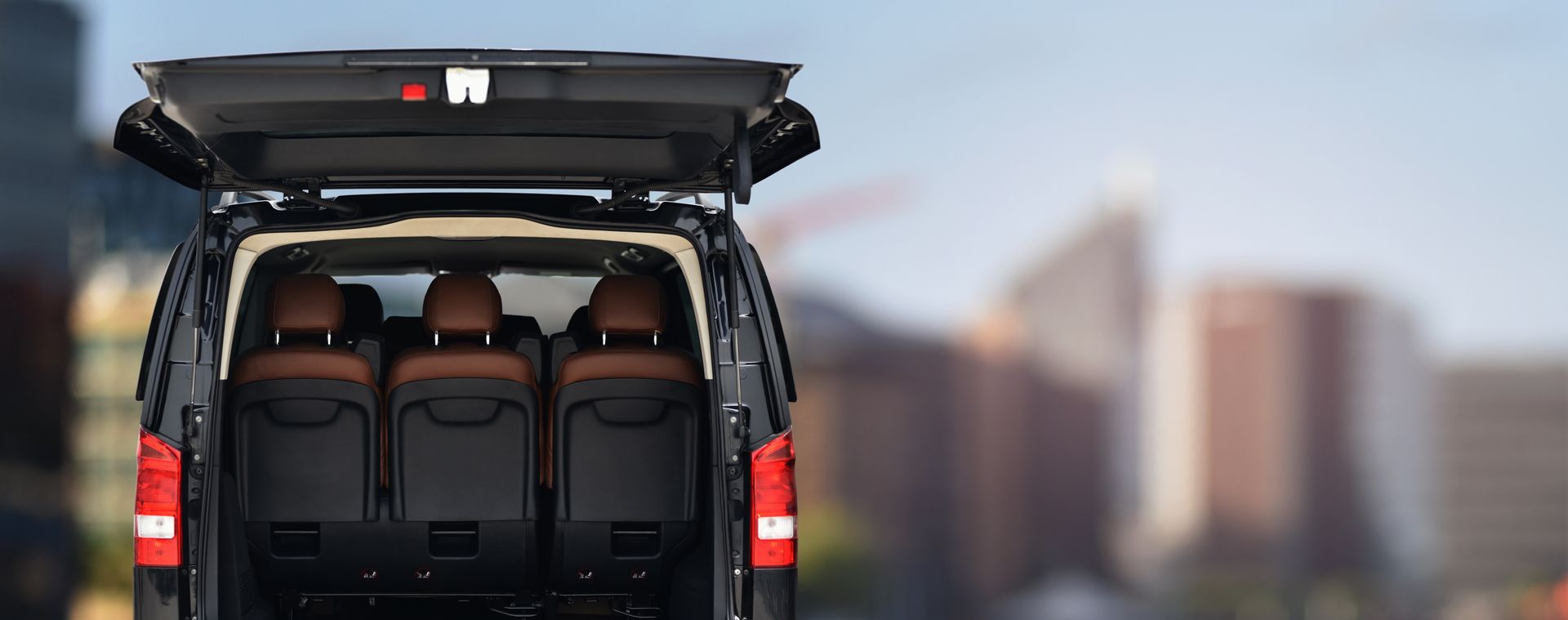 The back of a van with the trunk open and a city in the background.