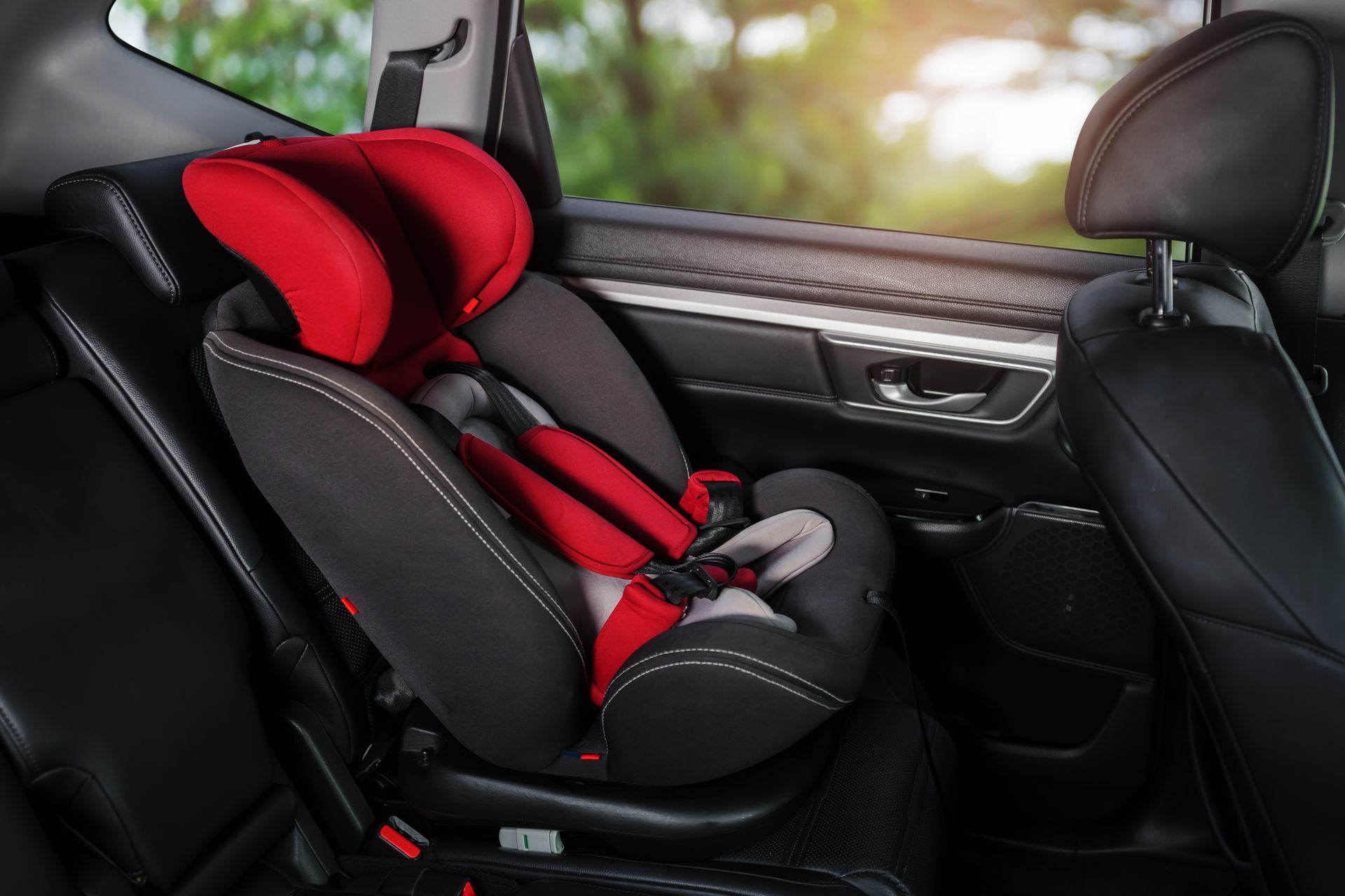 A red and black car seat is sitting in the back seat of a car.