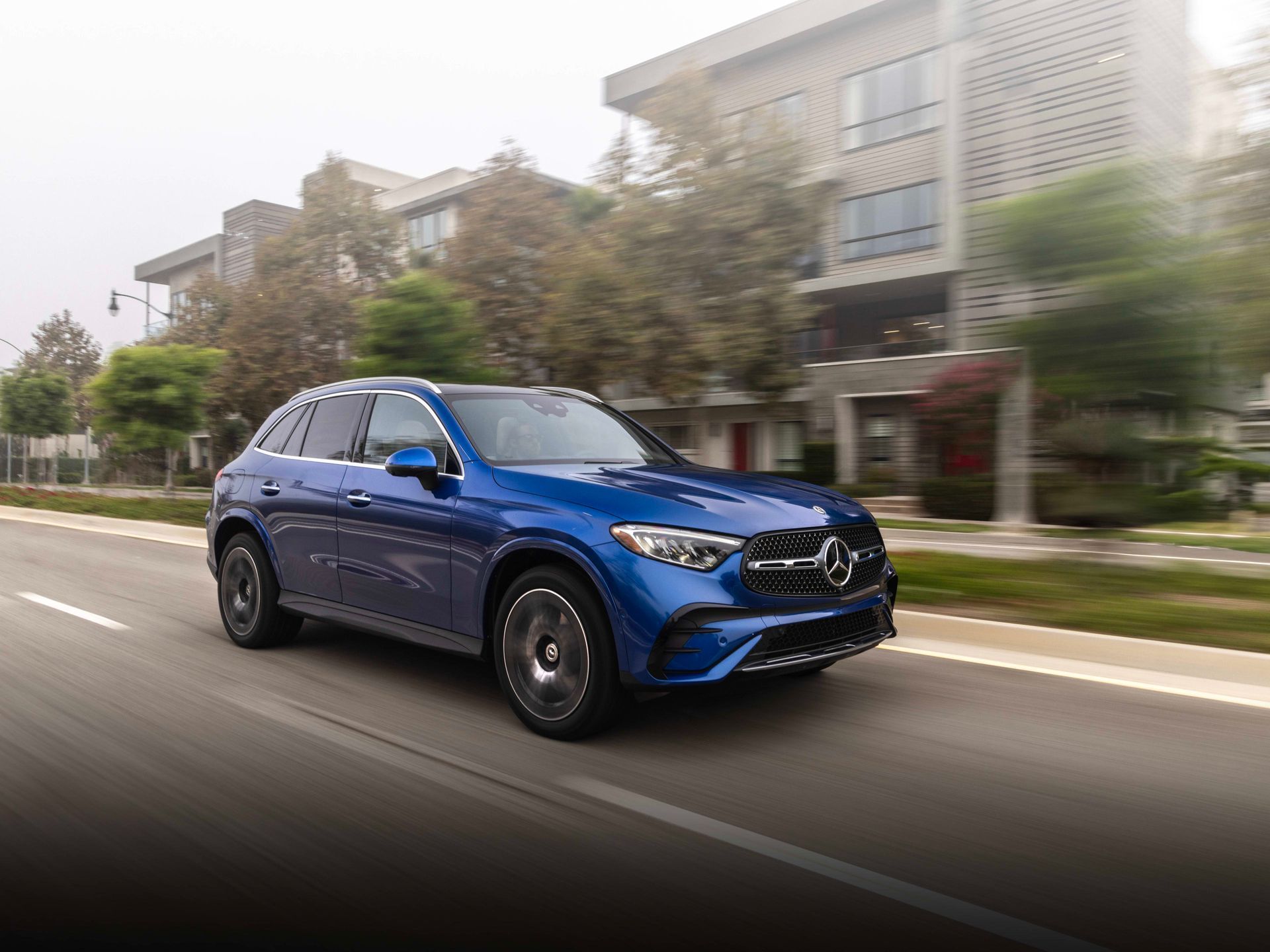 Blue SUV driving on a city street with motion blur and apartment buildings in the background